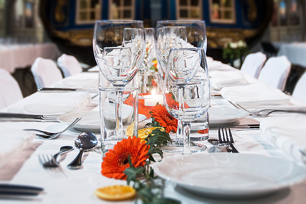 Festdukning. Bordet är smyckat med blommor. Vinglas, vattenglas, tallrikar, bestick och linneservetter. I förgrunden