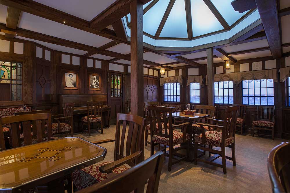 Viktorias röksalong. Mörk träpanel på väggarna. Träbord med glasskiva med stolar i trä med stoppad sits ställda runt.