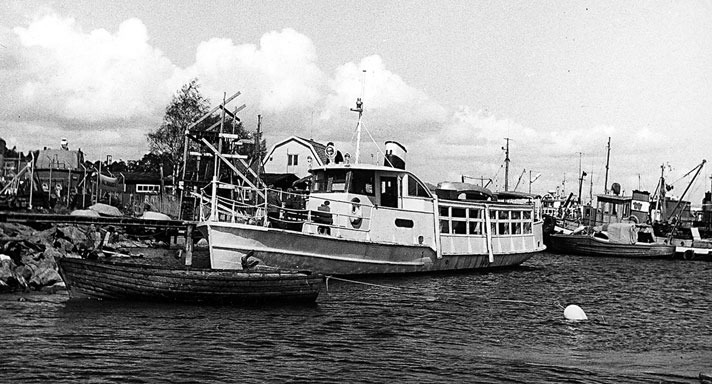 Flora är ett litet passagerarfartyg med salong i aktern och ett öppet fördäck. Fartyget är vitmålat och midskepps syns en styrhytt och bakom den en skorsten. På bilden ligger Flora vid en brygga i en mindre hamn. 
