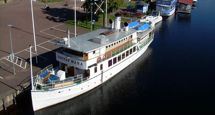 Gustaf Wasa är ett vitmålat passagerarfartyg med två däck med salonger. På taket syns en skorsten, två ventilatorer och två livbåtar. Längst fram på övre salongen syns kommandobryggan. På bilden ligger fartyget vid kaj i en hamnmiljö i Leksand. 
