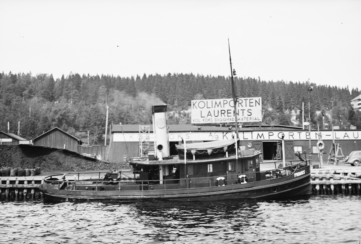 Primus är en svartmålad mindre bogserbåt. På överbyggnadens tak finns den ljusa skorstenen och en livbåt. På den svartvita bilden ligger fartyget vid kaj i Sundsvalls yttre hamn, i bakgrunden syns en magasinsbyggnad för kol. 