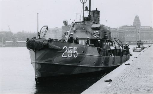 Sprängaren är en militär bogserbåt målad i kamouflagefärger. Det robusta skrovet har en överbyggnad och ovanför den sticker skorstenen upp. På den svartvita bilden ligger fartyget vid kaj i centrala Stockholm i bakgrunden syns Blasieholmen. Ombord syns matroser i Flottans uniform. I fören på barbordsida står det ”255” på skrovet.