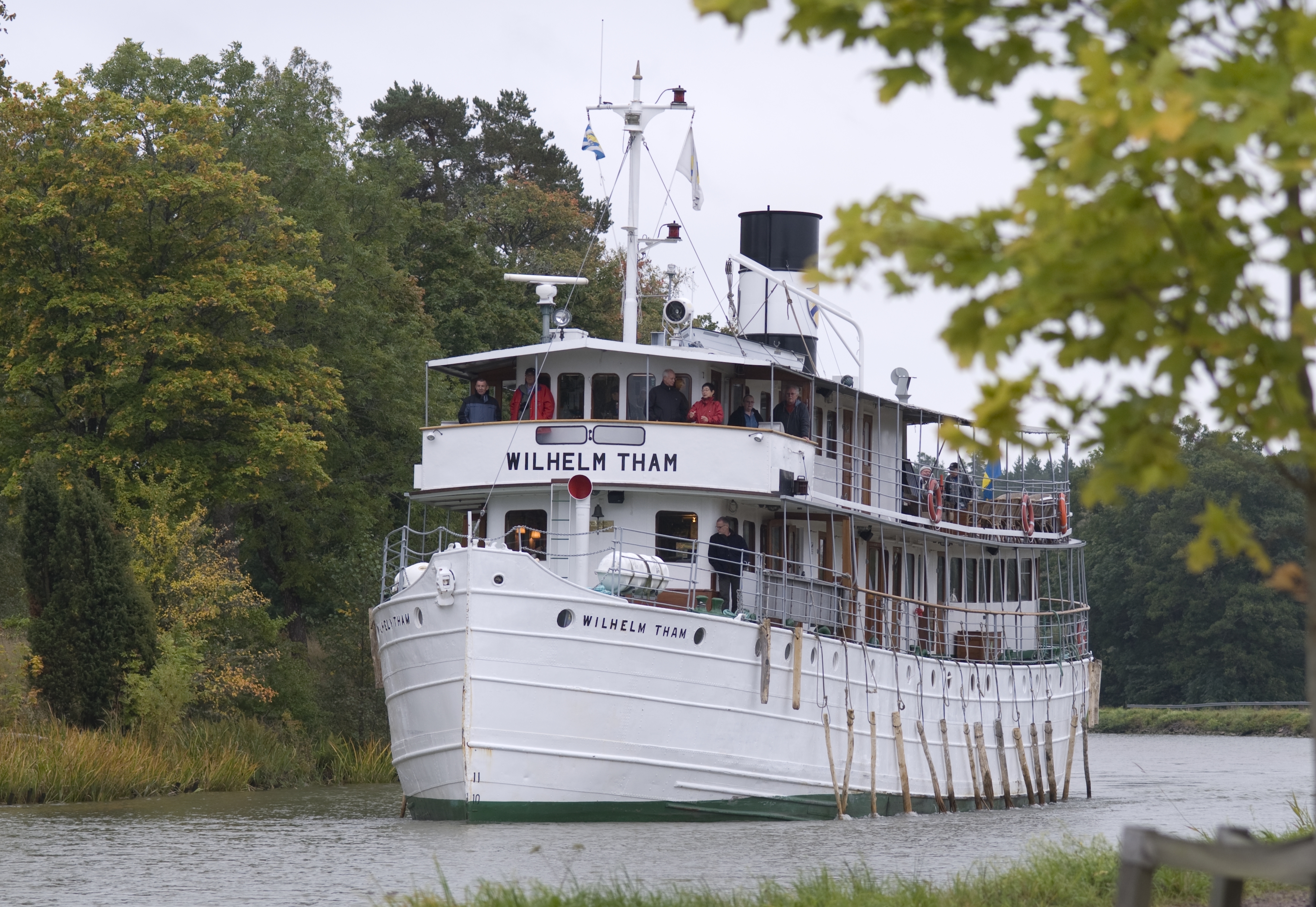 Wilhelm Tham är ett vitmålat passagerarfartyg med två salongsdäck. Det finns ett promenaddäck längs sidorna på båda däcken. Hon har en stor skorsten målad i svart och vitt. På bilden kör fartyget genom lövgrönskan i Göta kanal. 