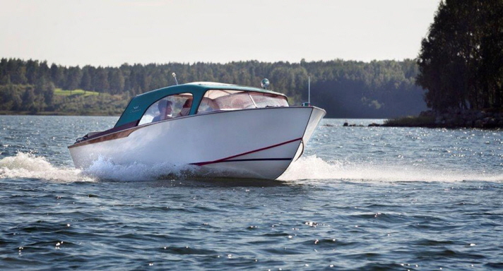 Coronet 18 Hard Top Sedan är en motorbåt med vitt skrov och en stor sittbrunn med turkosfärgad överbyggnad. Hon går för full fart i farleden.
