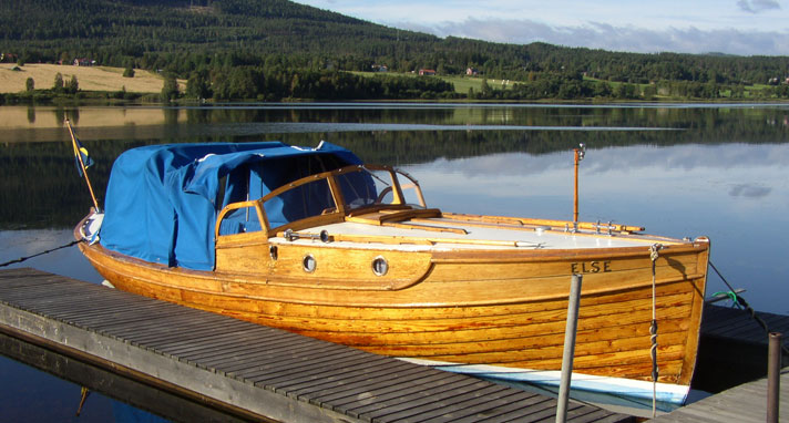 Else är en klinkbyggd trämotorbåt med två ventiler i förruffen längs med styrbordssida. Else har ett stort blått kapell med akterbågar över sittbrunnen. Båten ligger förtöjd vid en brygga. 