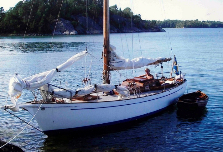 Fiorella är en segelbåt med vitt skrov. Seglen är revande och hon ligger för ankare vid en klippa. Vid I hennes akter guppar en liten jolle. En man syns ombord i sittbrunnen.