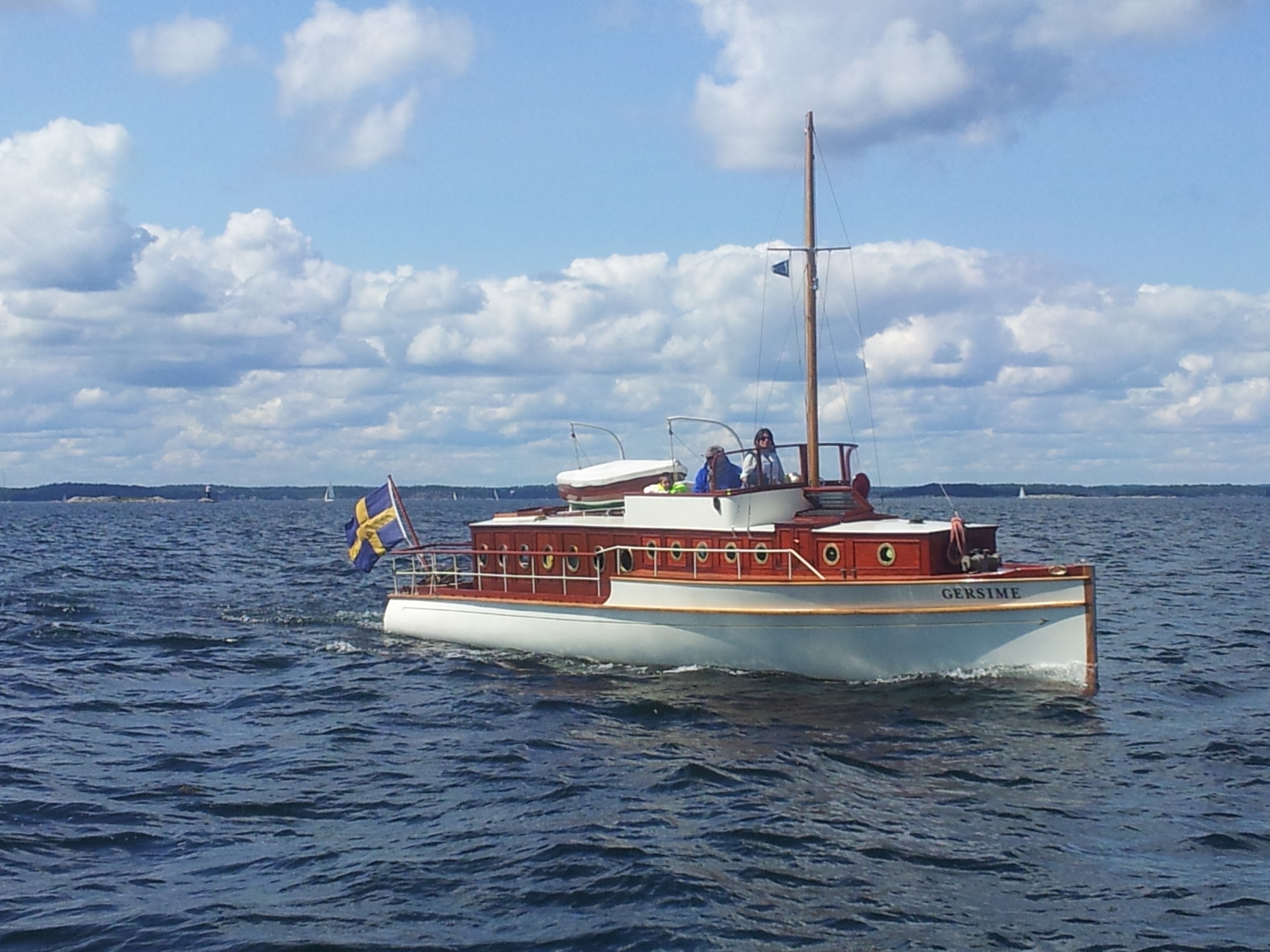 Gersime är en salongsmotorkryssare i mahogny med vitmålat skrov. Ovanför de främre salongsventilerna syns styrhytten och bakom den en jolle ovanpå salongstaket.